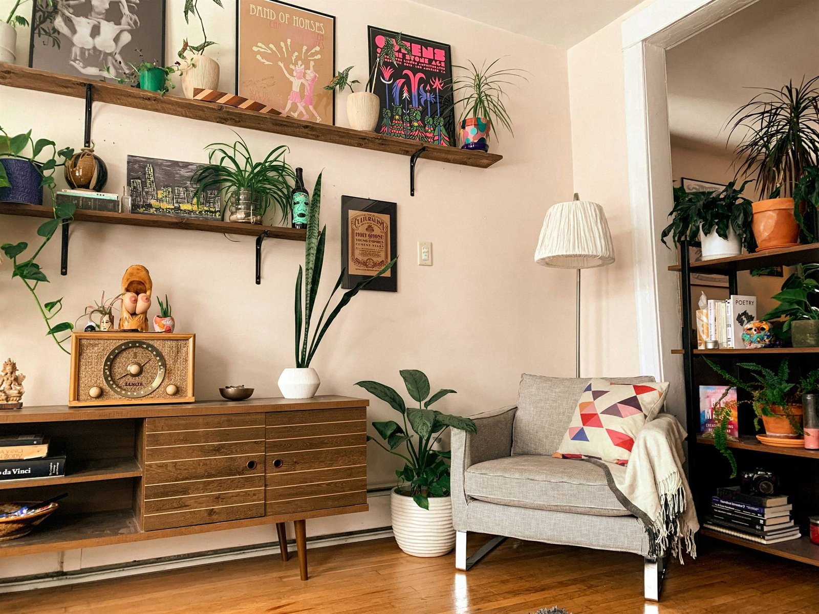 Estantes de madera con pósters, plantas, una radio antigua y un sillón gris