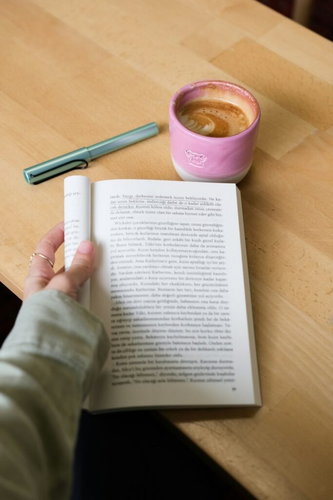 Una mano sostiene un libro abierto junto a una taza de café